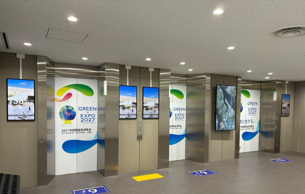 横浜市の庁舎のエレベーターホール。エレベーターの間の壁に、縦型のデジタルサイネージが複数設置されている